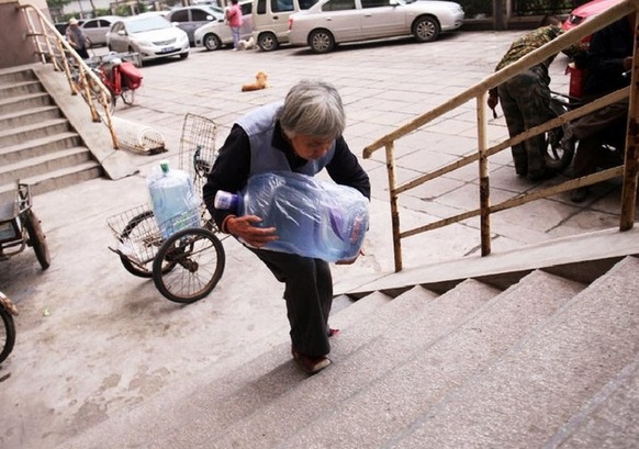 70岁的老人高美运正在吃力地搬运桶装水.