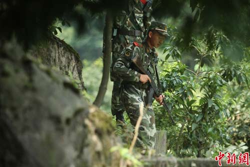 　图为武警官兵提着枪支搜寻犯罪嫌疑人踪迹。